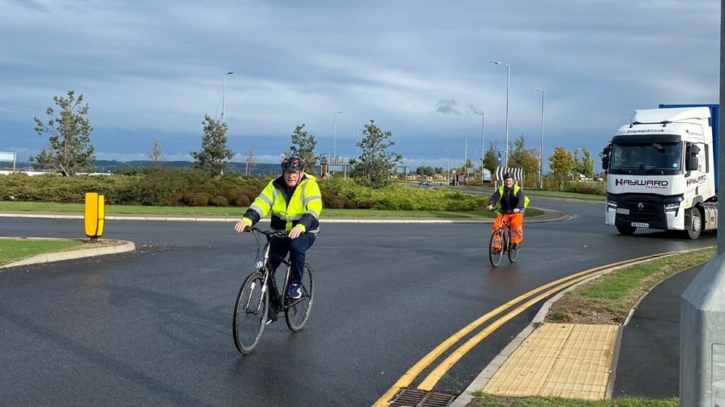 Two people riding bikes along a road wearing helmets